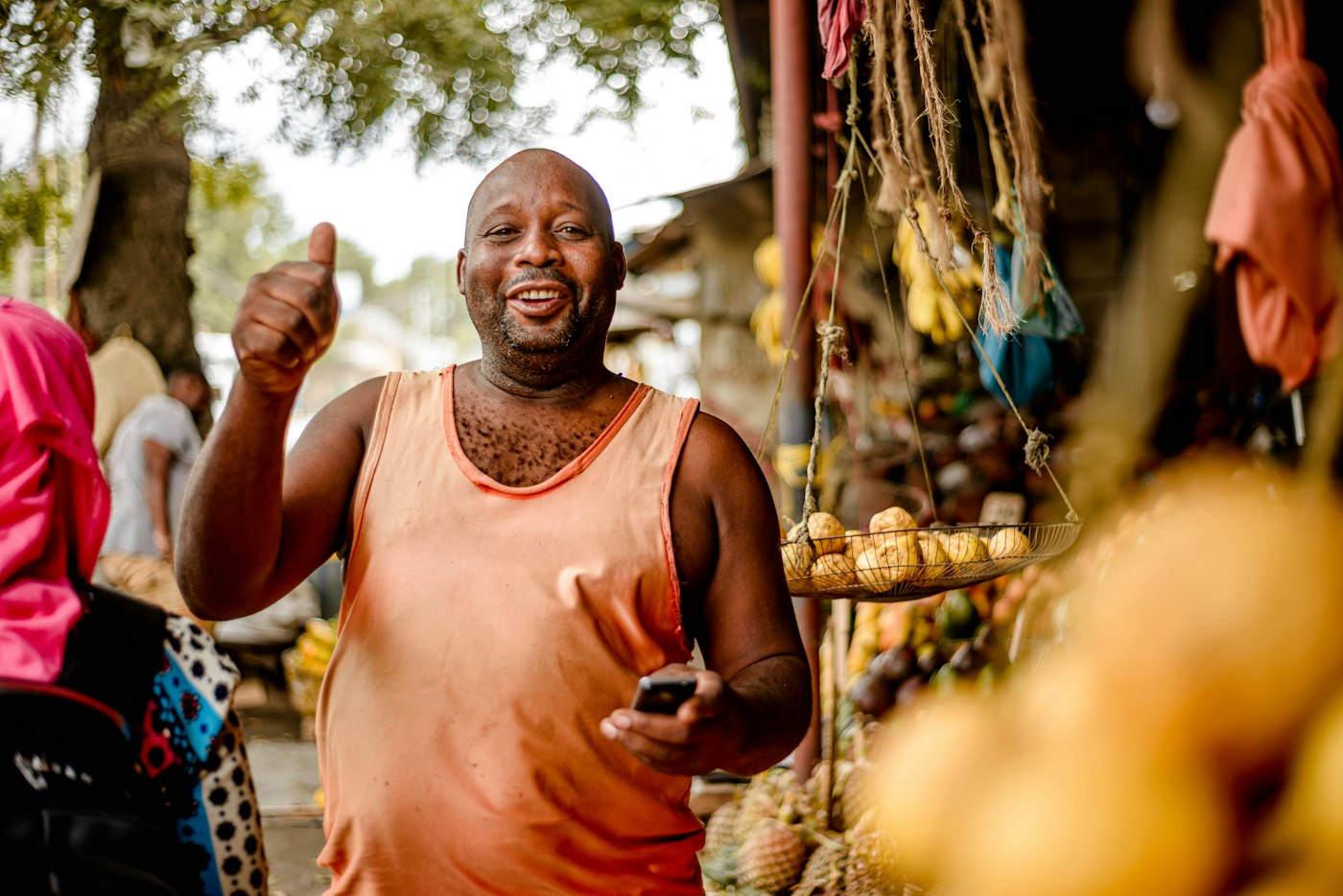 An African produce vendor using a mobile phone at his fruit stand